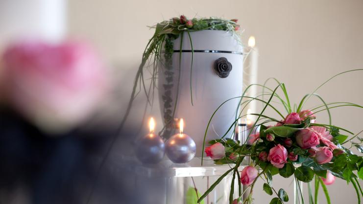 Blumenschmuck mit rosa Rosen und grünen Pflanzenarrangements auf einem Tisch, umgeben von Kerzen und einem weißen Behälter.