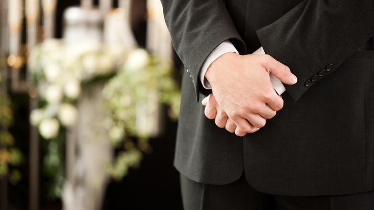 Ein Mann in einem Anzug steht mit verschränkten Händen vor einer dekorierten Kulisse mit Blumen und Kerzen.