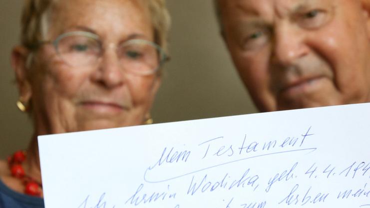 Nahaufnahme eines älteren Paares, das ein handgeschriebenes Testament auf Papier hält.